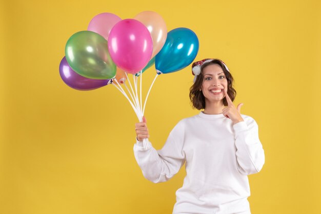 Front view young pretty female holding balloons on yellow desk christmas new year color woman emotion