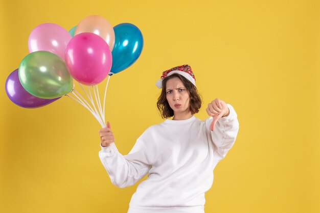Front view young pretty female holding colorful balloons on yellow emotion christmas new year woman color