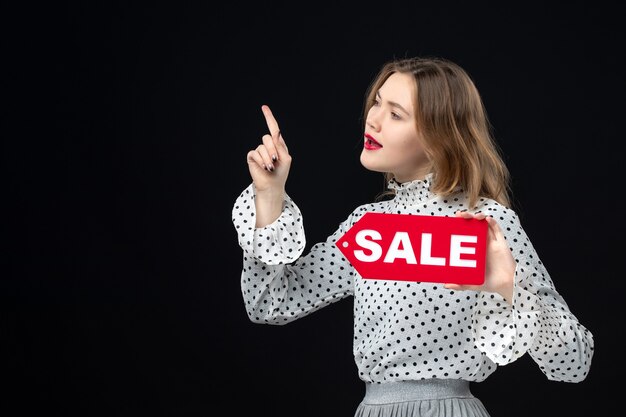 Front view young pretty female holding sale writing on black wall color shopping fashion photo woman red