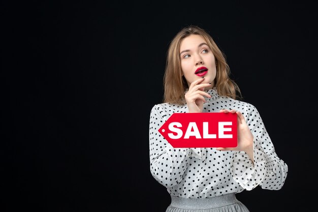 Front view young pretty female holding sale writing on black wall emotion red shopping photo woman color