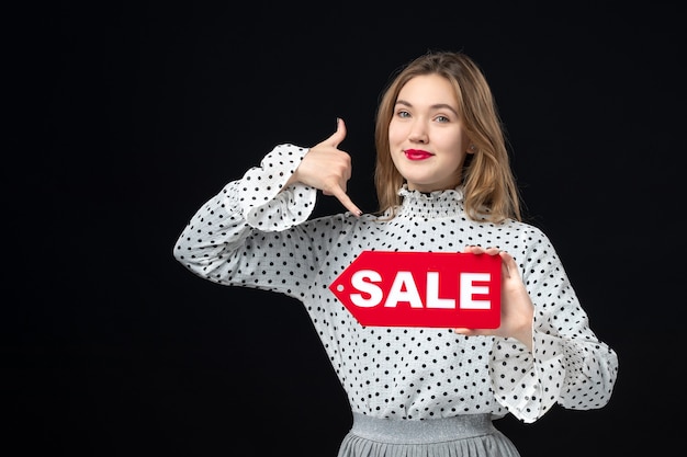 Front view young pretty female holding sale writing on black wall model beauty emotions red shopping fashion woman color