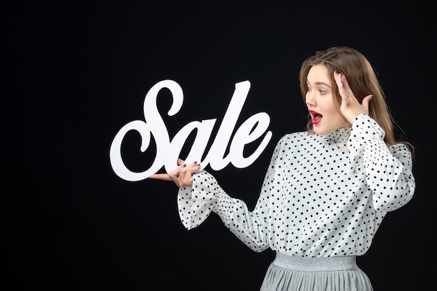 Front view young pretty female holding sale writing on a black wall shopping beauty fashion emotion color model photo