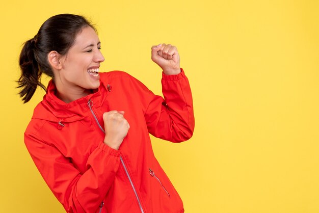 Front view young pretty female in red coat on yellow background