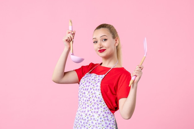 Free photo front view young pretty housewife in cape holding spoons on pink wall
