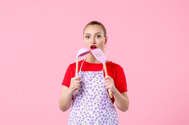 Front view young pretty housewife in cape holding spoons on pink wall