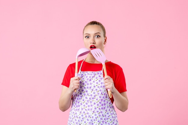 Front view young pretty housewife in cape holding spoons on pink wall