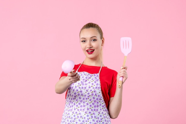 Front view young pretty housewife in cape with spoons on pink wall