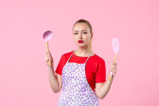 Front view young pretty housewife in cape with spoons on pink wall