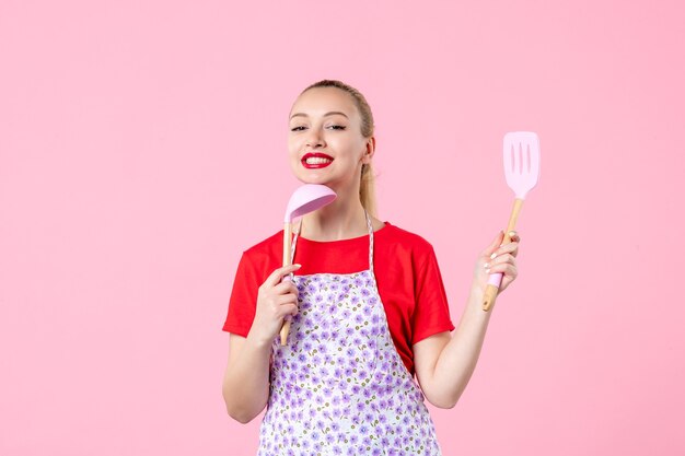 Front view young pretty housewife in cape with spoons on pink wall