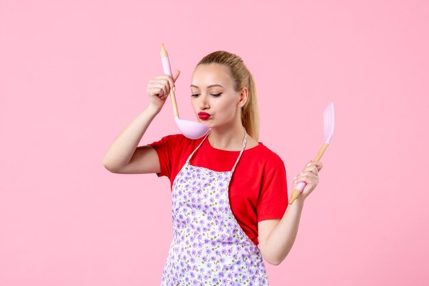 Front view young pretty housewife in cape with spoons on pink wall