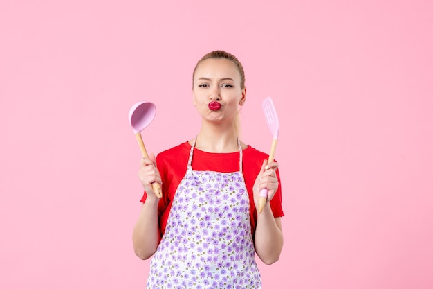 Front view young pretty housewife in cape with spoons on pink wall