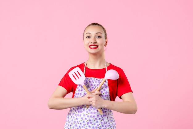 Front view young pretty housewife in cape with spoons on pink wall