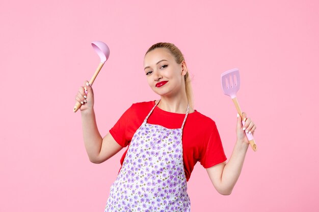 Front view young pretty housewife in cape with spoons on pink wall