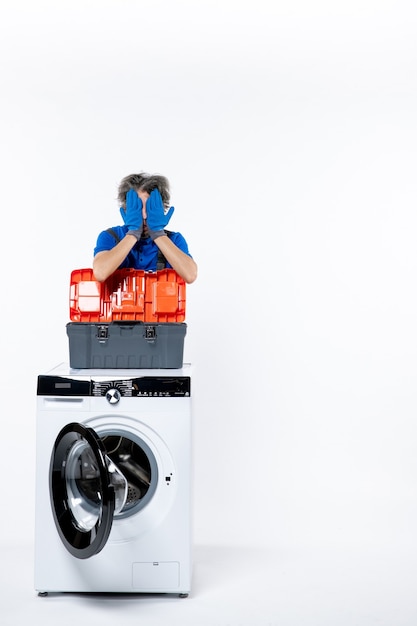 Free photo front view of young repairman covering his face with hands washing machine on white wall