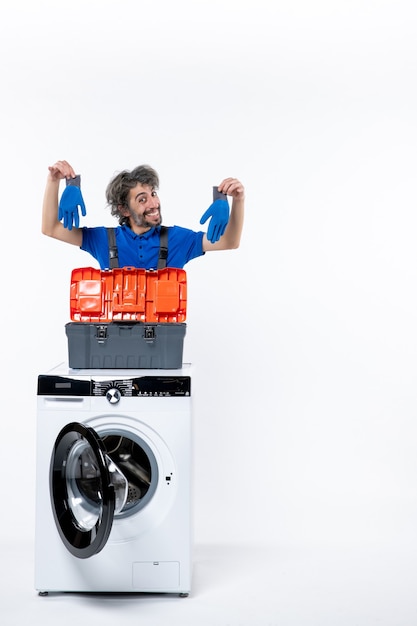 Free photo front view of young repairman holding blue gloves behind washing machine on white wall