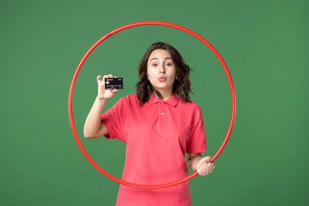 Front view young saleswoman holding hula hoop and bank card on green surface