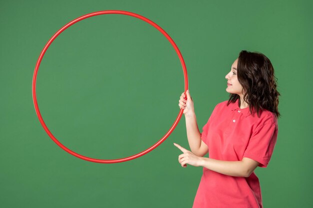 Front view young saleswoman holding red hula hoop on green surface