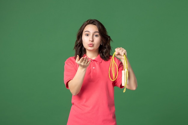 Front view young saleswoman holding skipping rope and sending kisses on green surface