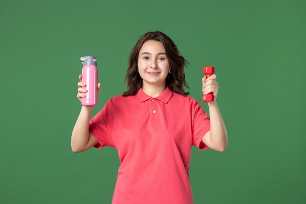 Front view young saleswoman holding thermos and dumbbell on green surface