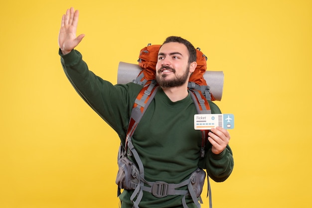 Free photo front view of young smiling travelling guy with backpack and showing ticket on yellow background