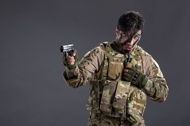 Free photo front view of young soldier in camouflage aiming gun on the dark wall