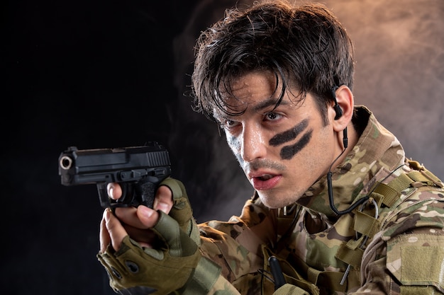 Vista frontale del giovane soldato in mimetica con pistola sul muro nero