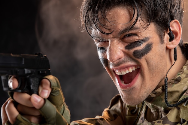 Front view of young soldier in camouflage with gun on black wall