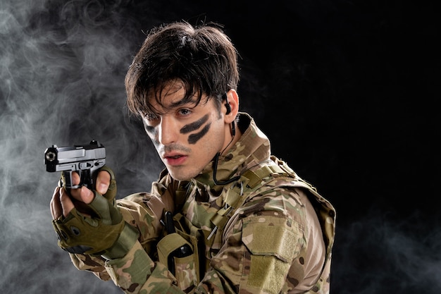 黒い壁に銃を持った迷彩の若い兵士の正面図