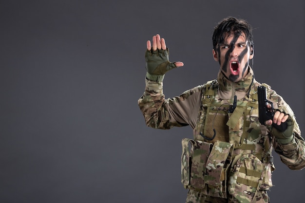 Free photo front view of young soldier in camouflage with gun on dark wall