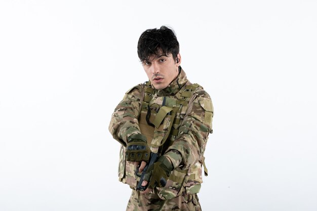 Вид спереди молодого солдата в камуфляже с пушкой на белой стене
