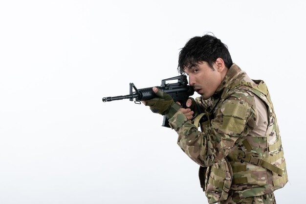 Front view young soldier fighting in camouflage with machine gun white wall