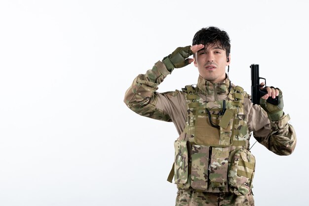 Вид спереди молодой солдат в военной форме с пистолетом на белой стене