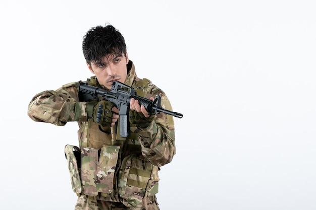 Вид спереди молодой солдат в военной форме с пулеметом на белой стене