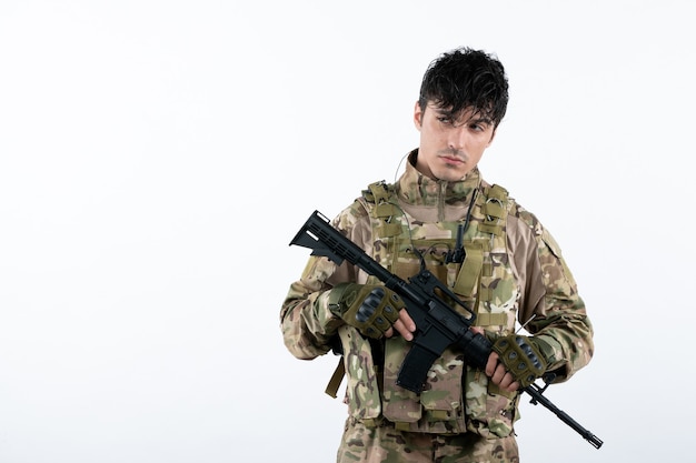 Front view of young soldier in military uniform with machine gun white wall