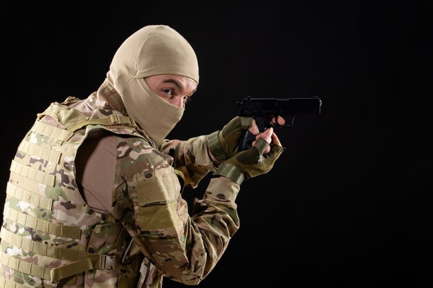 Front view young soldier in uniform aiming gun on a black wall