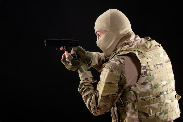 Front view young soldier in uniform aiming gun on black wall