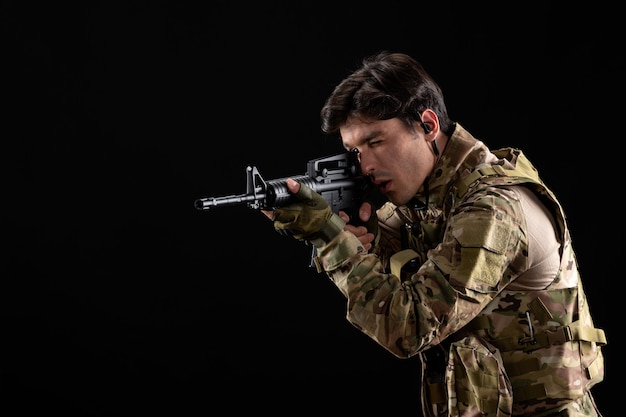 Front view young soldier in uniform aiming his rifle on black wall