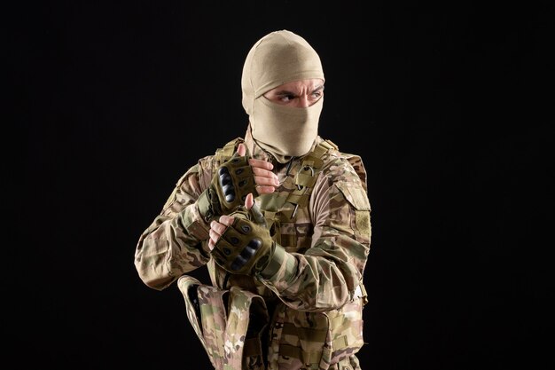 Вид спереди молодого солдата в форме и маске на черной стене