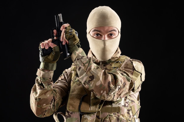 Front view of young soldier in uniform reloading gun on black wall