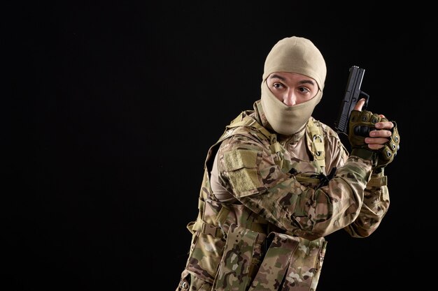 Front view young soldier in uniform with gun black wall