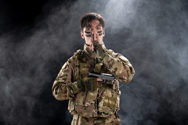黒い壁に銃を持った制服を着た若い兵士の正面図