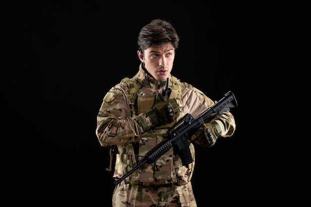 Foto gratuita fronte di vista giovane soldato in uniforme con fucile sul muro nero