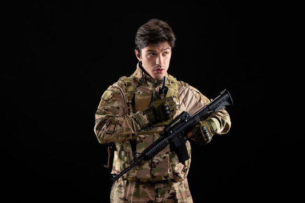 Front of view young soldier in uniform with rifle on the black wall