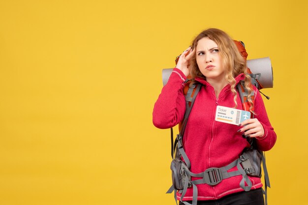 Front view of young thinking emotional travelling girl in medical mask holding ticket