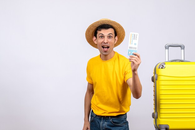 Front view young tourist standing near suitcase holding air ticket