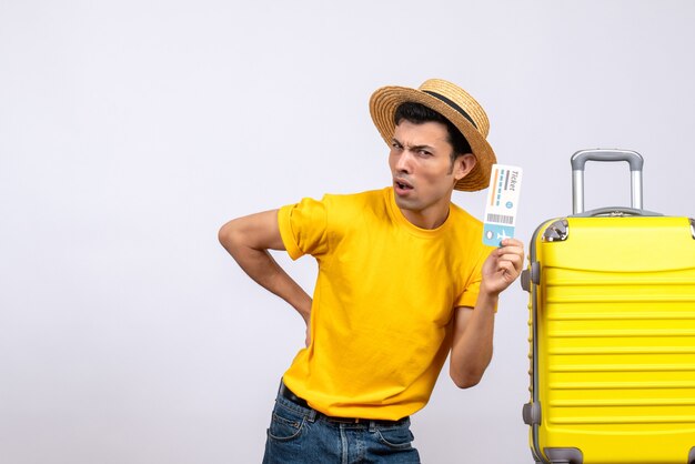 Front view young tourist standing near yellow suitcase holding ticket