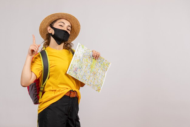 Front view young traveller with backpack holding up map pointing up