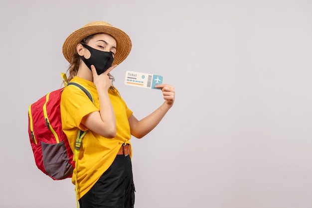 Front view young traveller with backpack holding up ticket putting hand on her chin