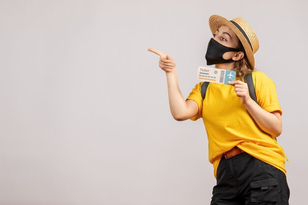 Front view young traveller with backpack wearing black mask holding travel ticket