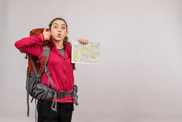 Вид спереди молодой путешественник с большим рюкзаком, держащий палец вверх, показывает карту